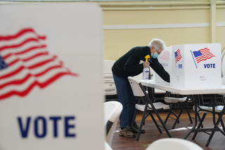 An election inspector at the Spiritual Renewal Center, wipes down a table after a voter leaves the seat to cast their vote.